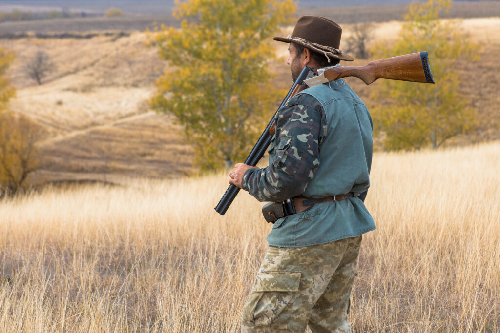 A hunter with a gun in his hands in hunting clothes in the autumn forest in search of a trophy. 