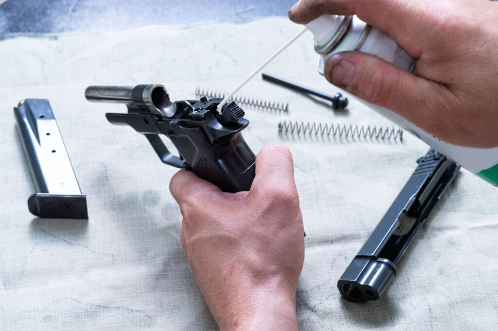 The gunsmith lubricates the mechanism of the pistol. Injection of lubricating oil through a straw. Master holds a gun and oil spray.