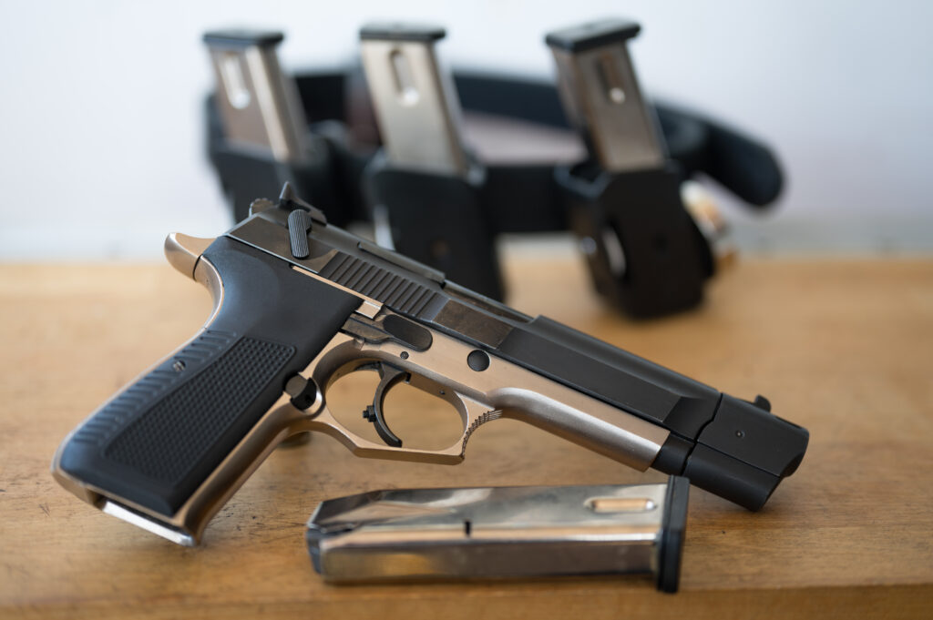 Detail of the 9mm pistol with a magazine in front of the IPSC belt with the magazines on. On top of a wooden table